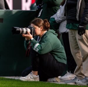 “Sports photographer kneeling on the sidelines taking photos during a youth soccer match.” Example of an ActionShot photographer